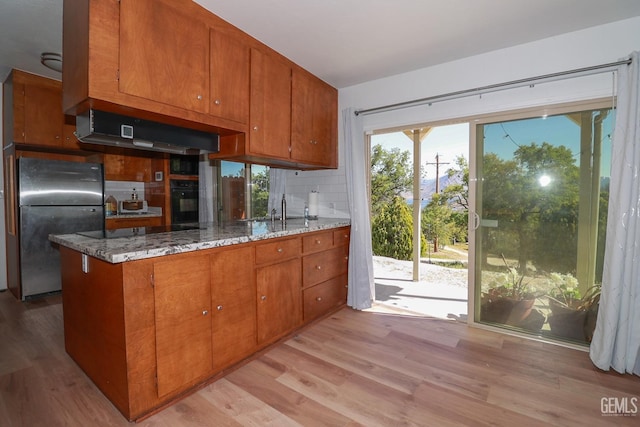 kitchen with stainless steel refrigerator, sink, tasteful backsplash, light stone counters, and light hardwood / wood-style floors