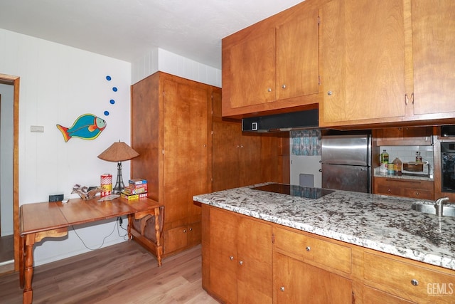 kitchen featuring black appliances, light hardwood / wood-style floors, and light stone countertops