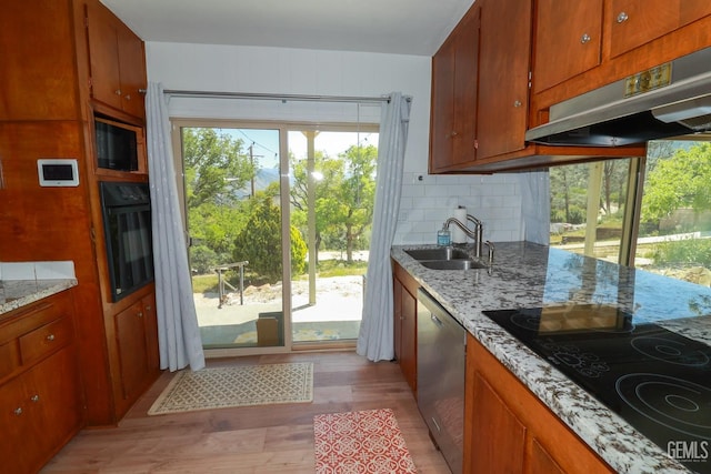 kitchen with black appliances, light wood-type flooring, light stone countertops, and sink