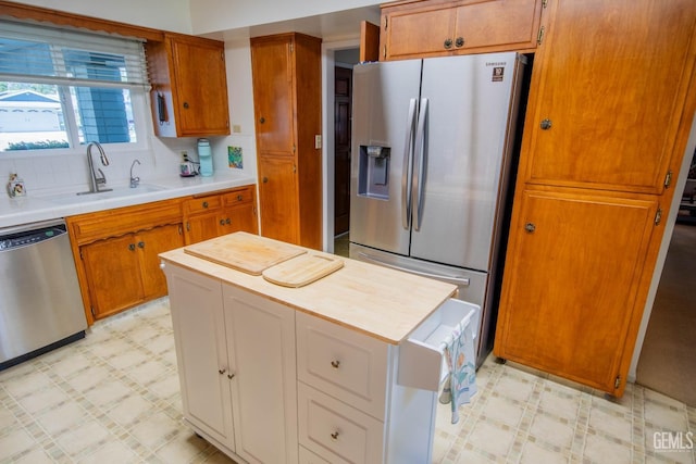 kitchen with brown cabinetry, light floors, appliances with stainless steel finishes, and a sink