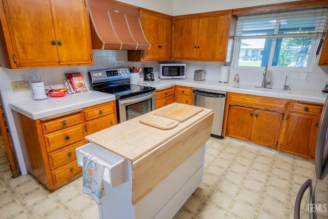 kitchen featuring a sink, tasteful backsplash, appliances with stainless steel finishes, wall chimney range hood, and light floors