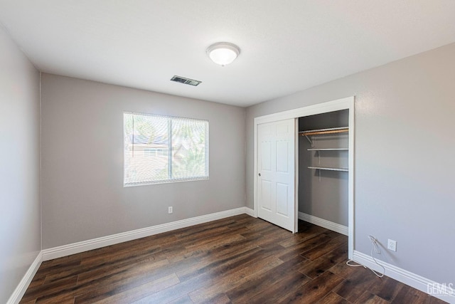 unfurnished bedroom featuring dark wood-style floors, baseboards, visible vents, and a closet