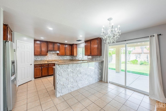 kitchen featuring backsplash, light tile patterned flooring, a peninsula, stainless steel fridge, and under cabinet range hood