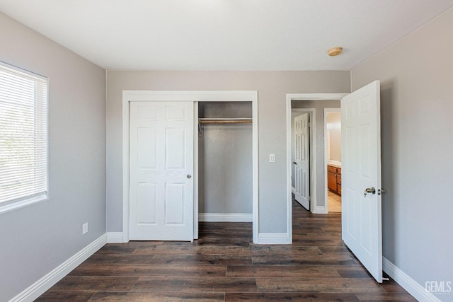 unfurnished bedroom with dark wood-type flooring, a closet, and baseboards