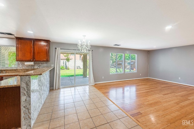 interior space with visible vents, baseboards, light wood finished floors, brown cabinetry, and an inviting chandelier