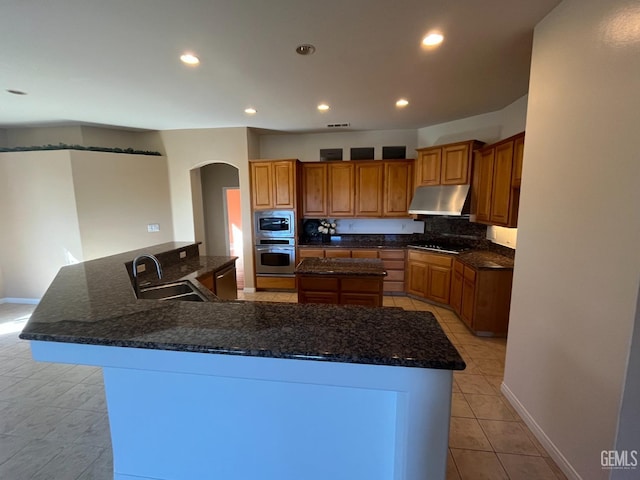 kitchen featuring under cabinet range hood, a spacious island, appliances with stainless steel finishes, and brown cabinetry