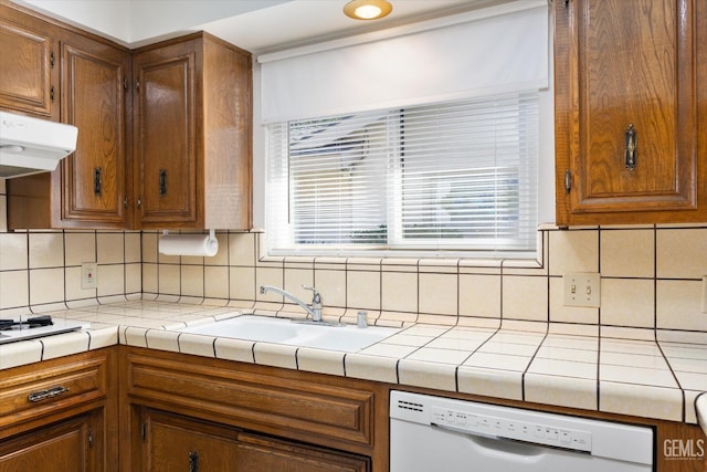 kitchen featuring white dishwasher, a sink, tile counters, and under cabinet range hood