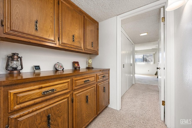 corridor with light carpet and a textured ceiling