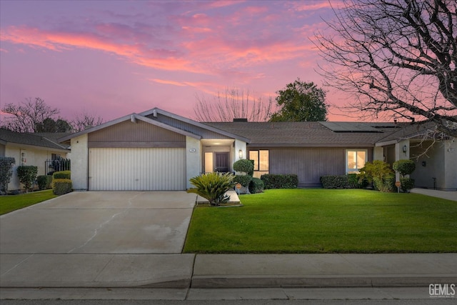 view of front of house featuring solar panels, a lawn, an attached garage, and driveway