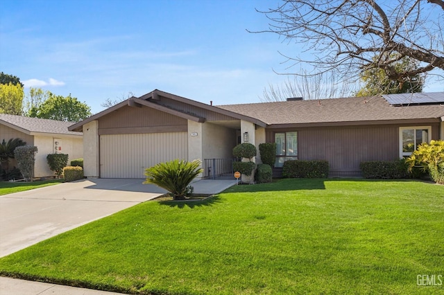 view of front of home featuring roof with shingles, an attached garage, roof mounted solar panels, driveway, and a front lawn