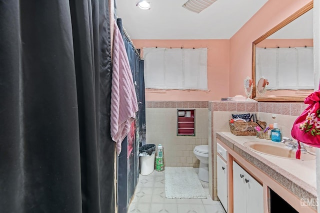 bathroom with vanity, toilet, and tile walls