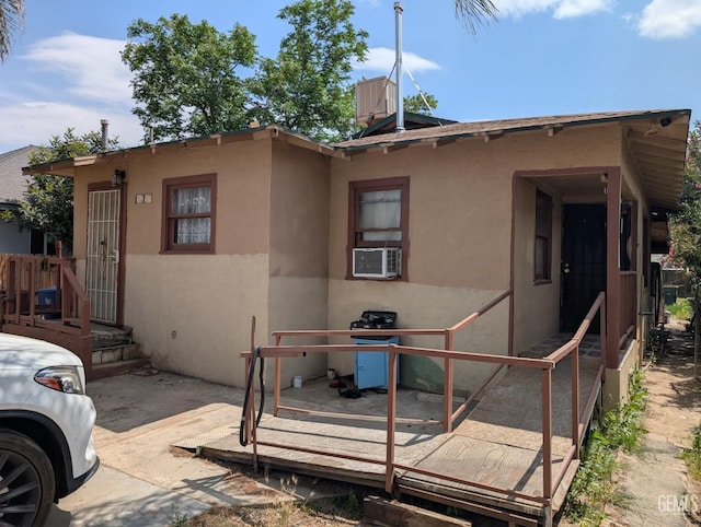 back of house with stucco siding, cooling unit, and a wooden deck