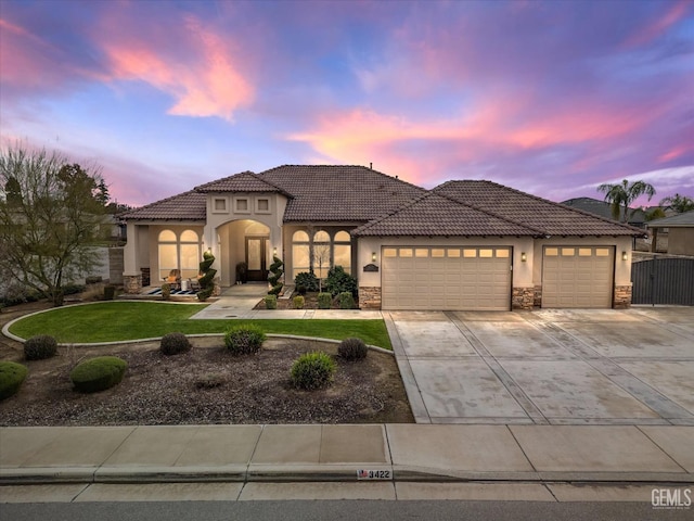 mediterranean / spanish-style home featuring a garage, concrete driveway, stone siding, a front lawn, and stucco siding