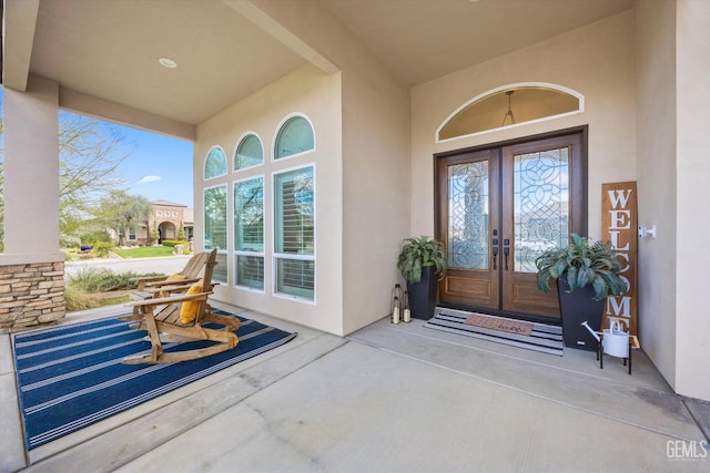 property entrance with stucco siding, covered porch, and french doors