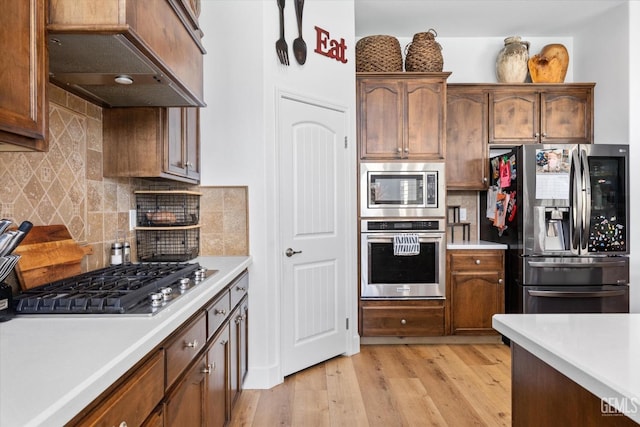 kitchen featuring under cabinet range hood, light wood-style floors, stainless steel appliances, and light countertops