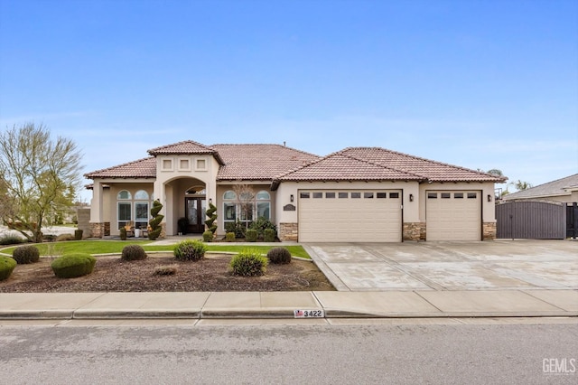 mediterranean / spanish-style house with driveway, a garage, stone siding, a gate, and stucco siding