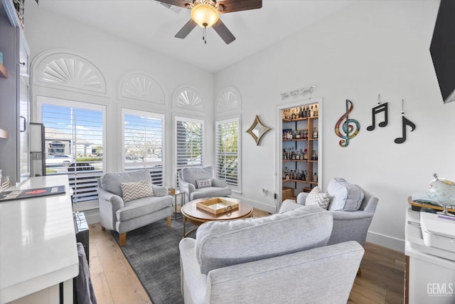 living area featuring wood-type flooring, baseboards, and a ceiling fan