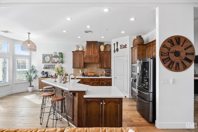 kitchen featuring visible vents, decorative backsplash, light wood-style flooring, appliances with stainless steel finishes, and custom exhaust hood