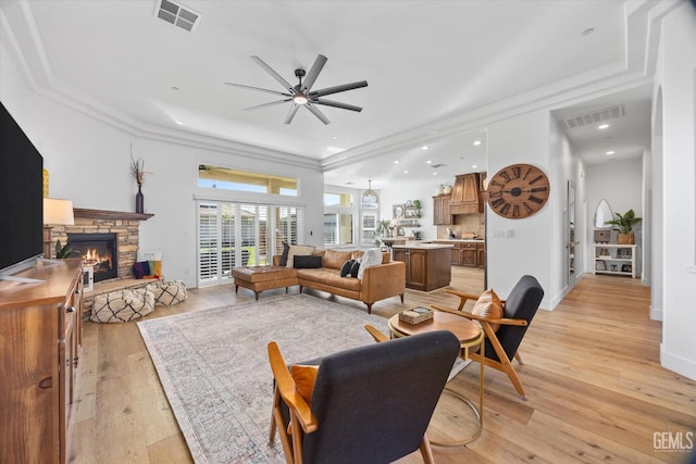 living room with light wood-type flooring, a fireplace, visible vents, and a ceiling fan