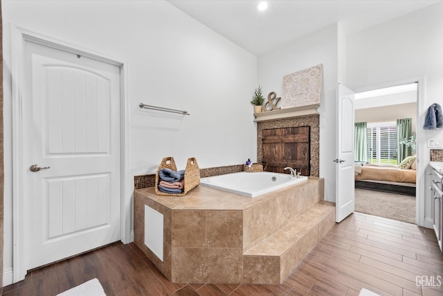 ensuite bathroom featuring wood finished floors, connected bathroom, and a bath