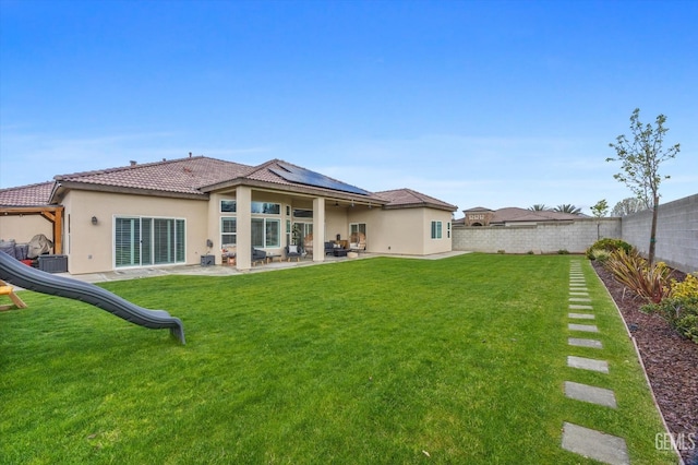 back of property featuring stucco siding, a lawn, roof mounted solar panels, a patio area, and a fenced backyard