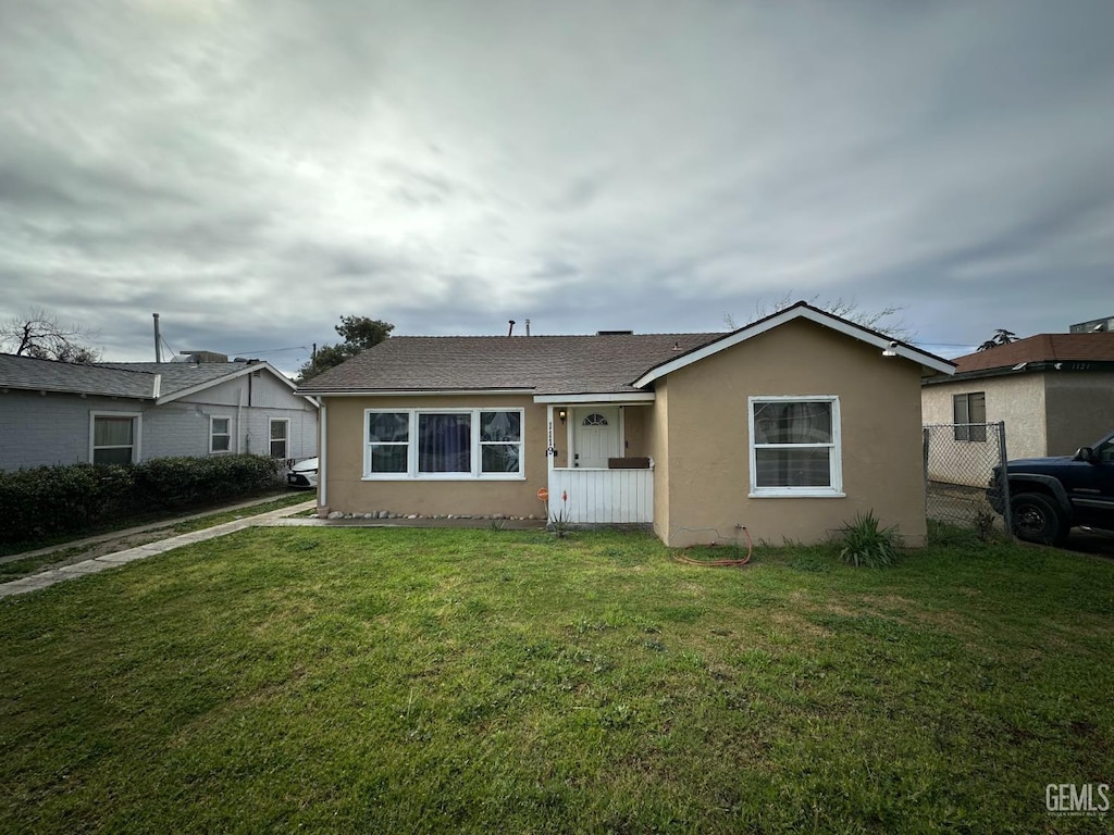 view of front facade featuring stucco siding, a front lawn, and fence