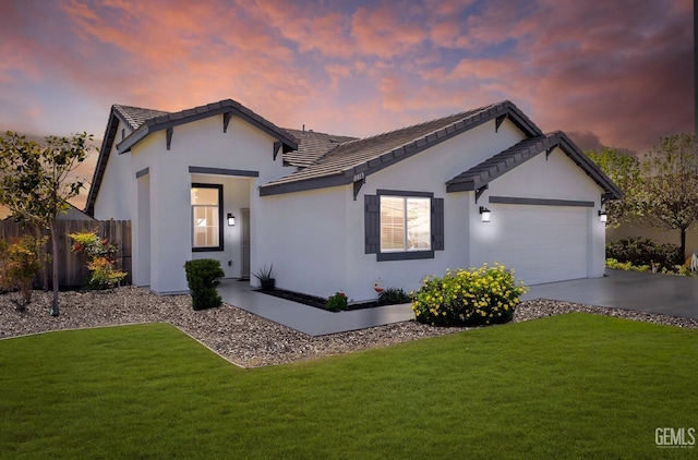 ranch-style home featuring an attached garage, fence, concrete driveway, stucco siding, and a front lawn