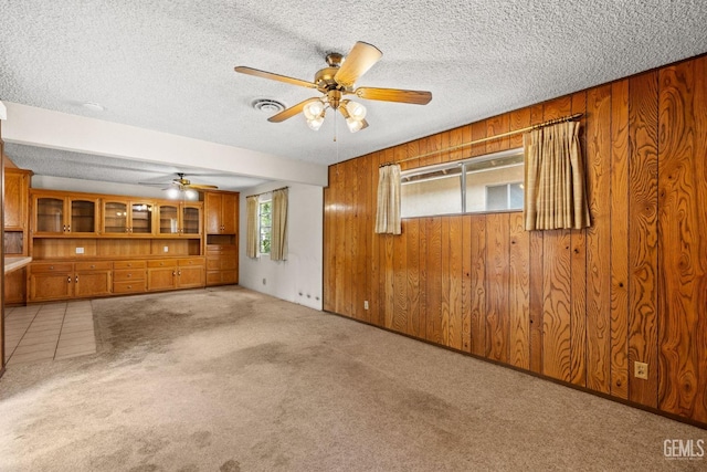 unfurnished living room featuring visible vents, ceiling fan, wooden walls, a textured ceiling, and carpet