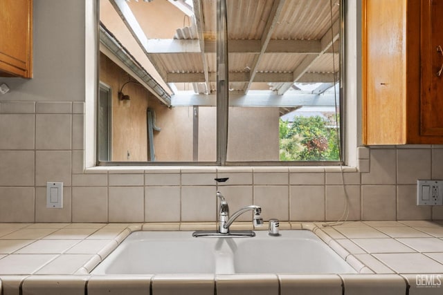 kitchen with tile counters, a skylight, decorative backsplash, and a sink
