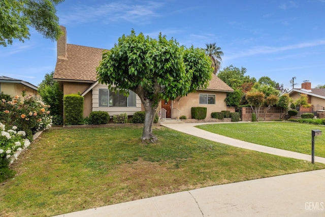 view of property hidden behind natural elements with a chimney, fence, a front lawn, a shingled roof, and stucco siding