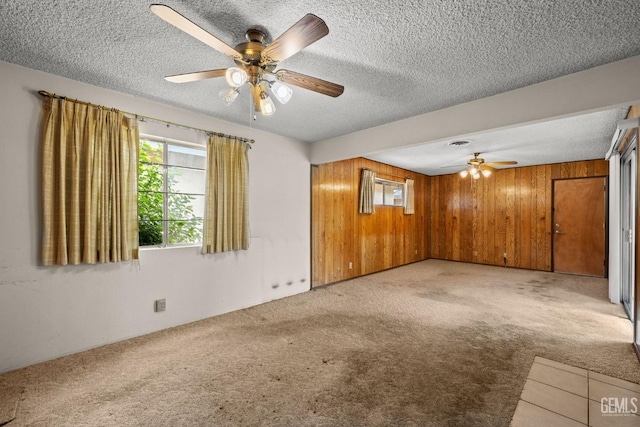 carpeted empty room with a textured ceiling, ceiling fan, and wood walls
