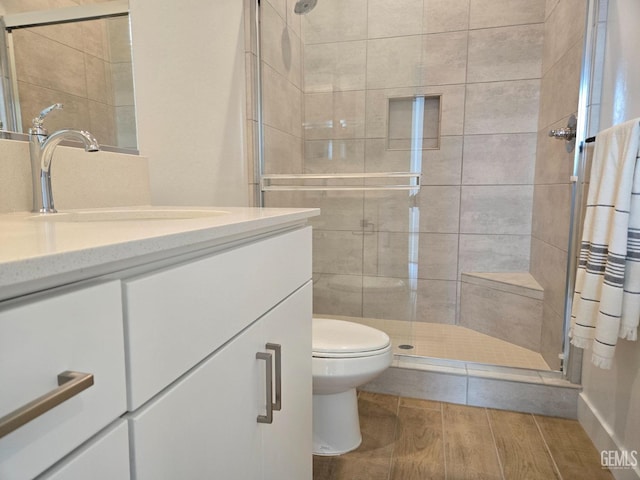 bathroom featuring wood finish floors, a shower stall, vanity, and toilet