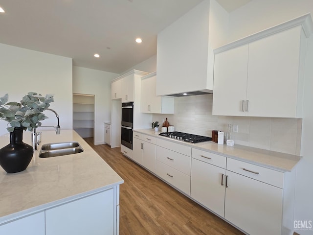 kitchen featuring light wood finished floors, a sink, light countertops, stainless steel gas stovetop, and backsplash