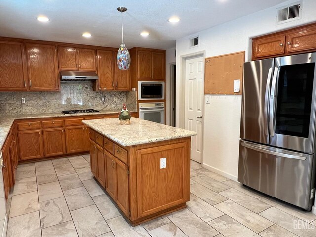 7412 Indian Gulch St, Bakersfield, CA 93313 - kitchen with appliances with stainless steel finishes, under cabinet range hood, brown cabinetry, a kitchen island, and light stone counters