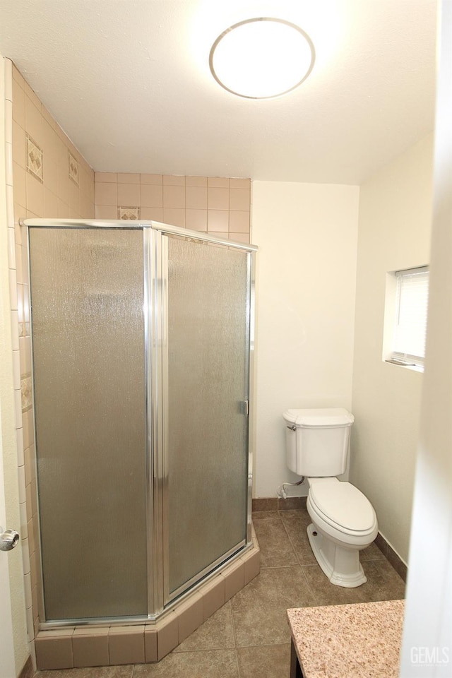 bathroom with toilet, a stall shower, baseboards, and tile patterned flooring