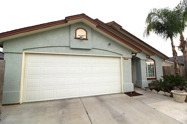 view of front facade with a garage, driveway, fence, and stucco siding