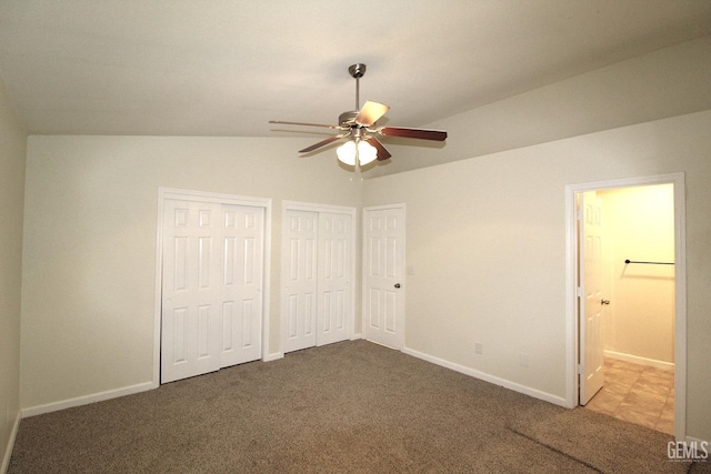 unfurnished bedroom featuring baseboards, vaulted ceiling, ensuite bath, carpet floors, and multiple closets