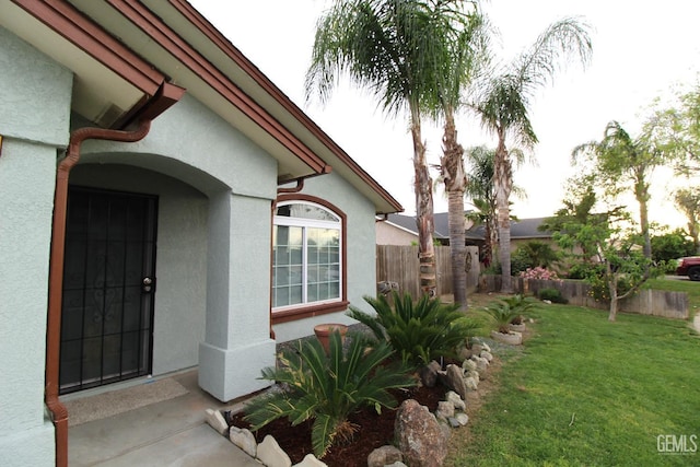 view of exterior entry with stucco siding, fence, and a lawn