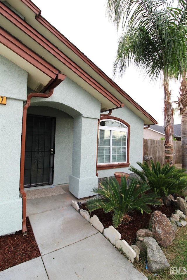 entrance to property featuring fence and stucco siding