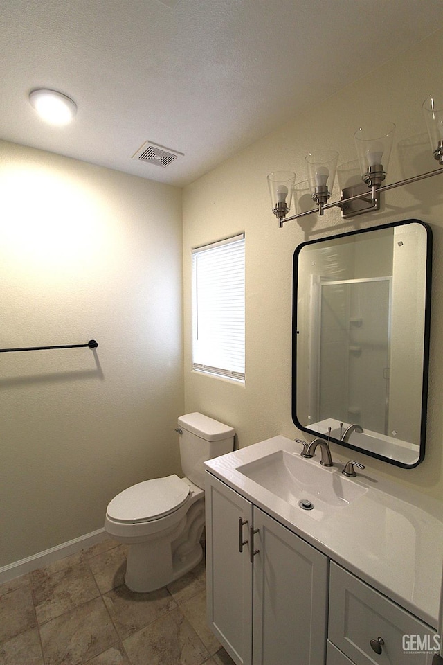 bathroom with vanity, visible vents, toilet, a stall shower, and baseboards