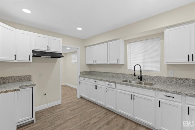 kitchen featuring light stone counters, light wood-type flooring, white cabinetry, and sink