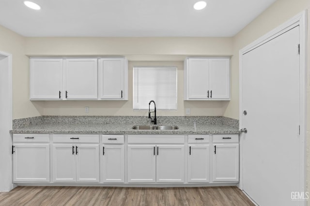 kitchen with white cabinets, light stone counters, and sink