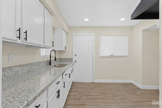 kitchen with light hardwood / wood-style floors, light stone countertops, white cabinetry, and sink