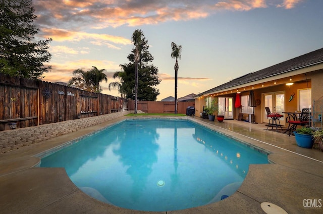 pool at dusk with a patio area, a fenced backyard, and a fenced in pool