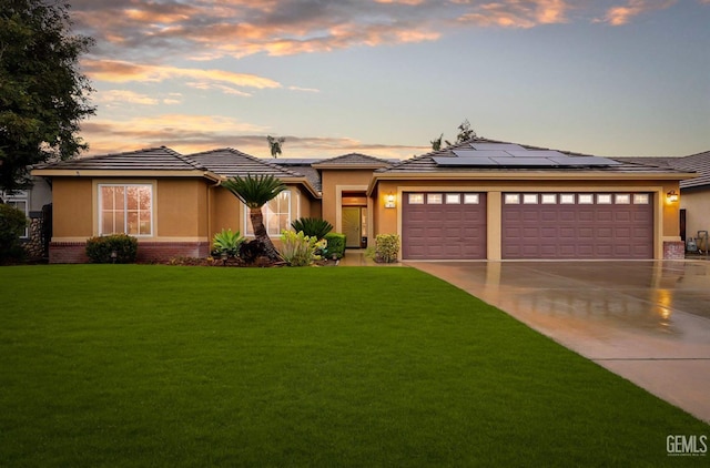 prairie-style house with a garage, brick siding, concrete driveway, a lawn, and roof mounted solar panels