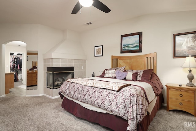 carpeted bedroom featuring arched walkways, visible vents, ceiling fan, and a tile fireplace