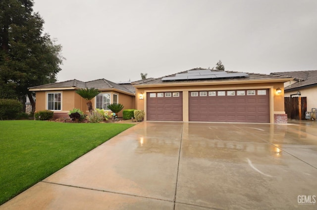 view of front of property with a garage, solar panels, driveway, stucco siding, and a front yard