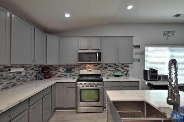 kitchen featuring light stone countertops, appliances with stainless steel finishes, vaulted ceiling, and gray cabinetry