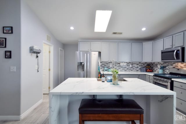 11712 Novara Ave, Bakersfield, CA 93312 - kitchen featuring appliances with stainless steel finishes, gray cabinets, backsplash, light stone counters, and baseboards