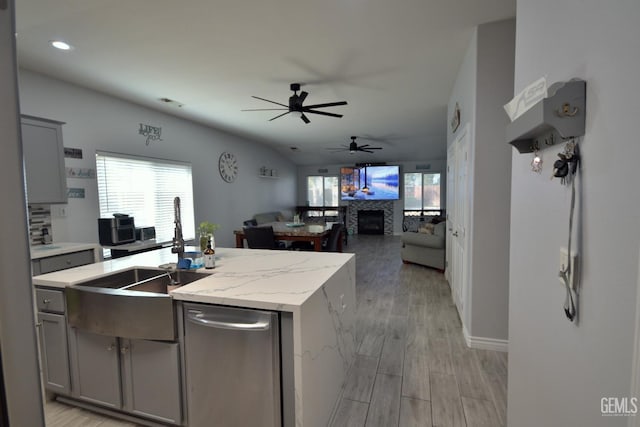 kitchen featuring gray cabinetry, a center island with sink, a stone fireplace, sink, and light hardwood / wood-style flooring